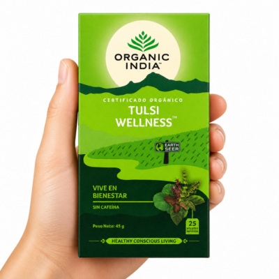 Caja de infusión Organic India Tulsi Wellness sostenida por una mano neutra sobre fondo blanco, té ayurvédico orgánico sin cafeína para el bienestar, equilibrio y relajación.