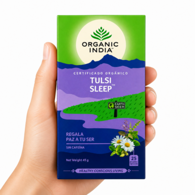 Caja de infusión Organic India Tulsi Sleep sostenida por una mano neutra sobre fondo blanco, té ayurvédico orgánico sin cafeína para dormir mejor y favorecer la relajación nocturna.