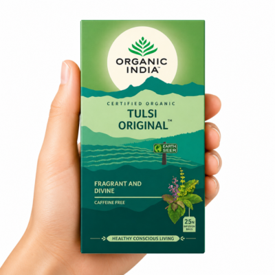 Infusión Organic India Tulsi Original sostenida por una mano neutra sobre fondo blanco, té ayurvédico orgánico sin cafeína para el bienestar diario