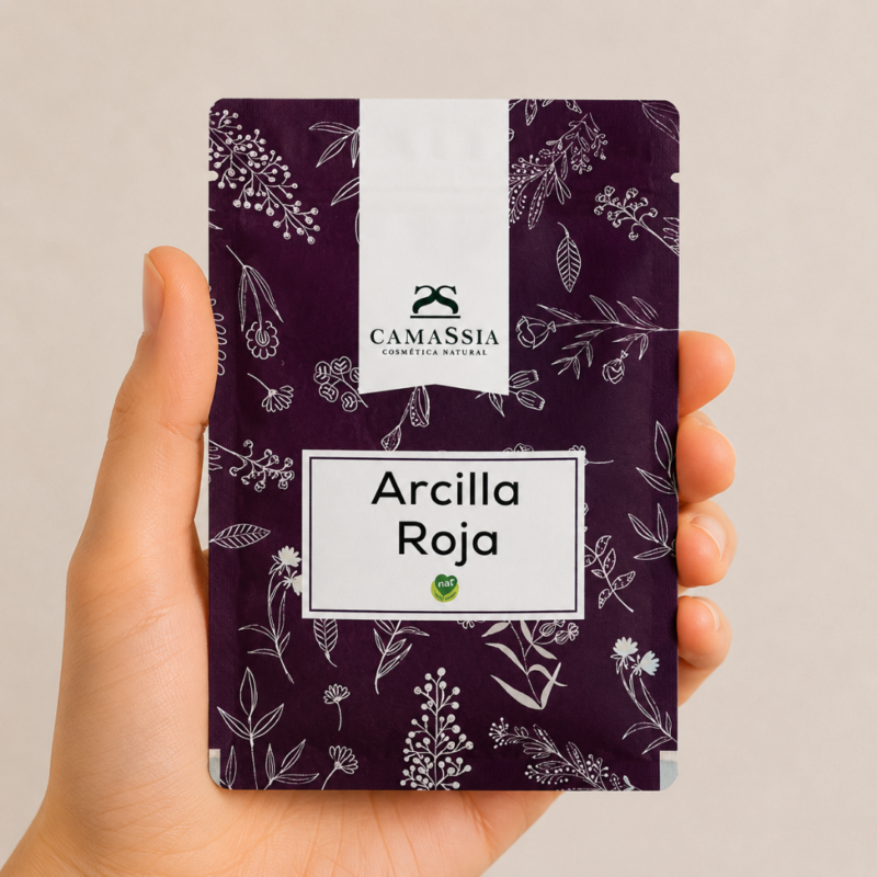 Mano neutra sosteniendo Arcilla Roja de Camassia sobre fondo claro minimalista.