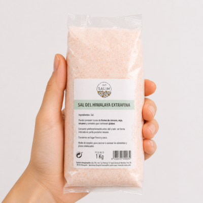 Mano neutra sosteniendo bolsa de Sal Extrafina del Himalaya Int Salim sobre fondo blanco minimalista.