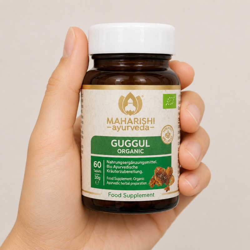Mano sosteniendo suplemento ayurvédico Guggul Organic de Maharishi Ayurveda en envase marrón con etiqueta verde y dorada