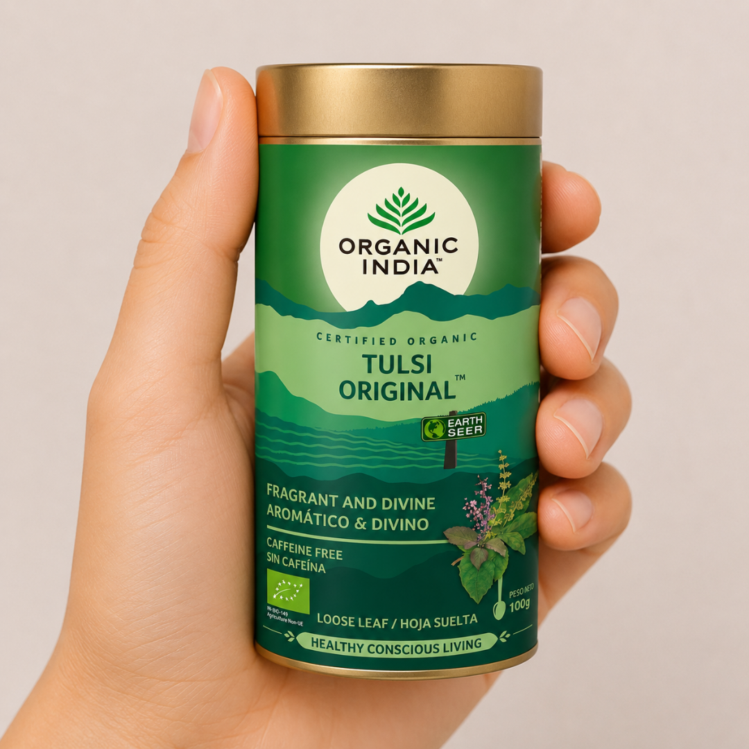 Tulsi Original Hojas Sueltas 100g Mano neutra sosteniendo envase de Tulsi Original Organic India en hojas sueltas sobre fondo beige minimalista.