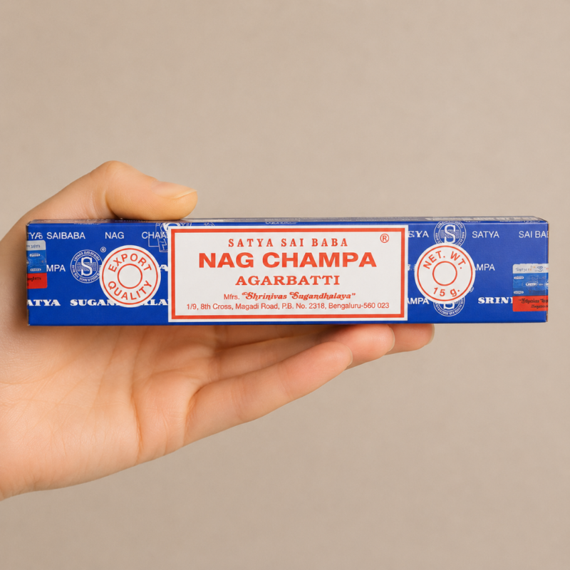 Mano neutra sosteniendo incienso Satya Nag Champa Agarbatti sobre fondo beige minimalista.