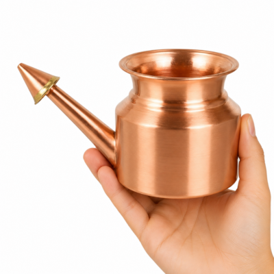 Lota nasal de cobre para limpieza nasal ayurvédica Jala Neti sostenida por una mano sobre fondo blanco.
