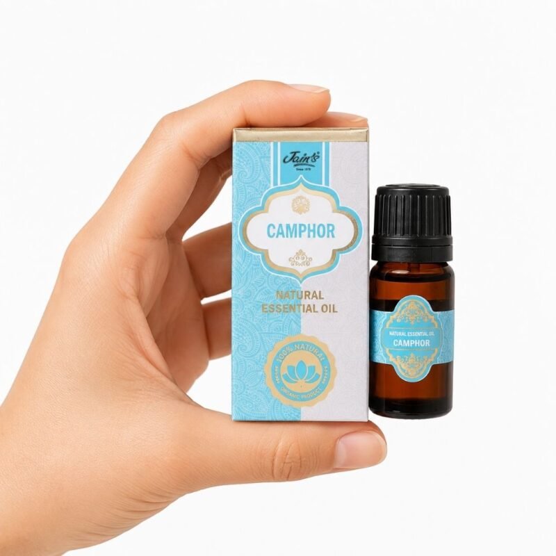 * Mano sosteniendo el Aceite Esencial de Alcanfor Jains junto a su caja original sobre fondo blanco.
