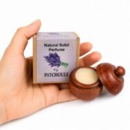 Mano sosteniendo el Perfume Sólido Patchouli Jains de 6 g con envase de madera y caja original sobre fondo blanco.