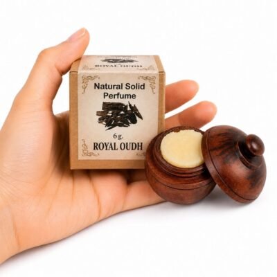 Mano sosteniendo el Perfume Sólido Royal Oudh Jains de 6 g con envase de madera y caja original sobre fondo blanco.