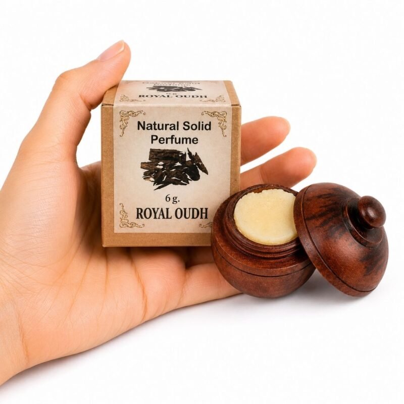 Mano sosteniendo el Perfume Sólido Royal Oudh Jains de 6 g con envase de madera y caja original sobre fondo blanco.