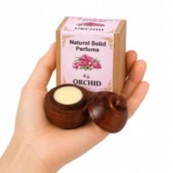 Mano sosteniendo el Perfume Sólido Natural Orchid Jains de 6 g con envase de madera y caja original sobre fondo blanco.