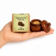 Mano sosteniendo el Perfume Sólido Amber de Jains de 6 g con envase de madera y caja original sobre fondo blanco.