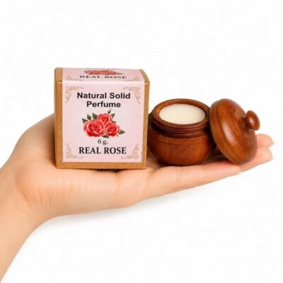 Mano sosteniendo el Perfume Sólido Real Rose de Jains de 6 g con envase de madera y caja original sobre fondo blanco.