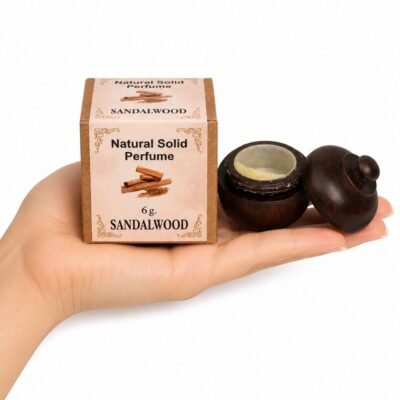 Mano sosteniendo el Perfume Sólido Sandalwood de Jains de 6 g con envase de madera y caja original sobre fondo blanco.