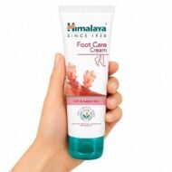 Crema para el Cuidado de Pies Foot Care Cream de Himalaya sostenida en una mano sobre fondo blanco