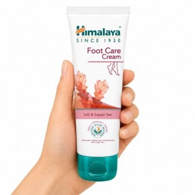 Crema para el Cuidado de Pies Foot Care Cream de Himalaya sostenida en una mano sobre fondo blanco