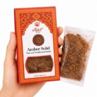 Mano sosteniendo Amber Solid Resin de Jain’s con caja y resina aromática tradicional sobre fondo blanco