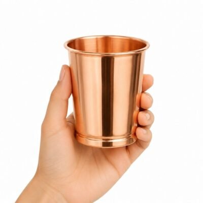 Vaso de cobre liso ayurvédico sostenido en una mano sobre fondo blanco