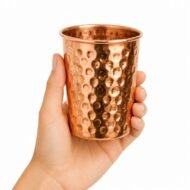 Vaso de cobre martillado ayurvédico sostenido en una mano sobre fondo blanco