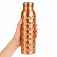 Botella de cobre martillada ayurvédica sostenida en una mano sobre fondo blanco